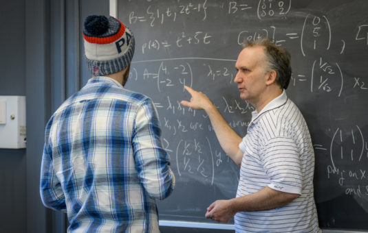 michael starz looking over whie board with student