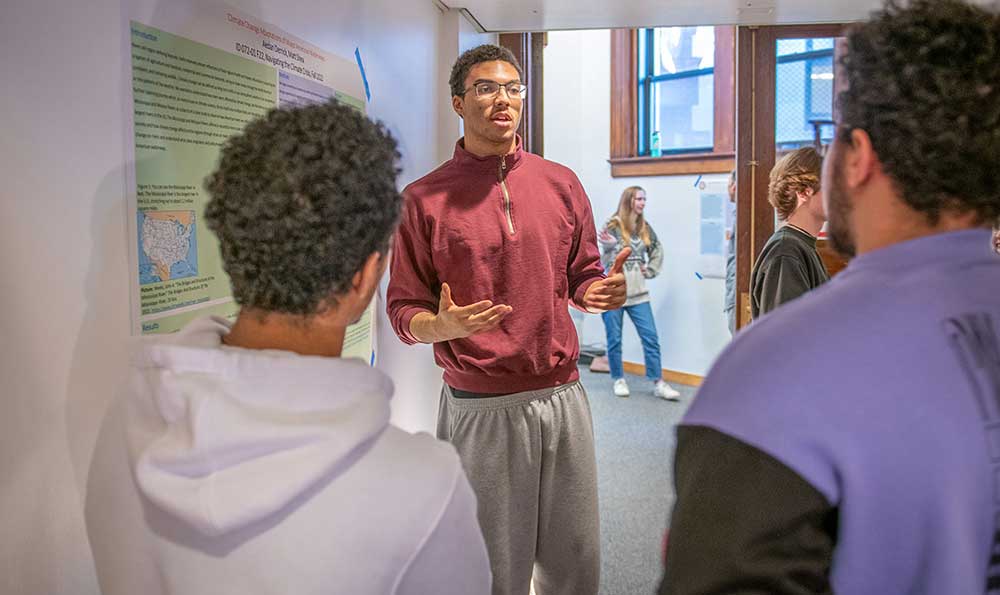 Aedan Derrick ’26, center and Matt Shea ’26, left, present their research project,  “Climate Change Adaptations of Major American Waterways,” at the poster salon that culminated their first-year intensive course.
