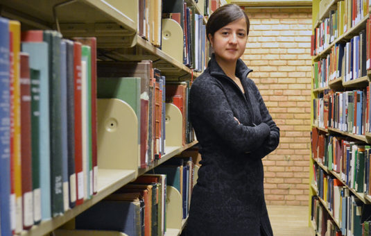 Student standing in book stacks in library